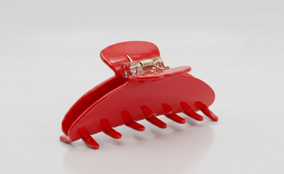 A bright red acetate hair claw clip with a small gold metal spring and hinge, shown on a clean white background.